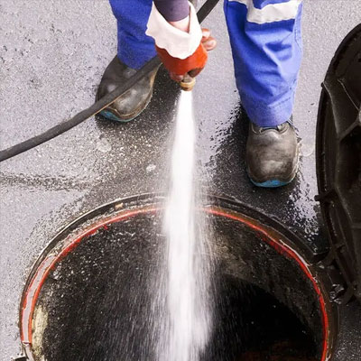 Worker spraying water down manhole