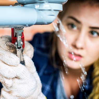 woman using wrench on leaky pipe