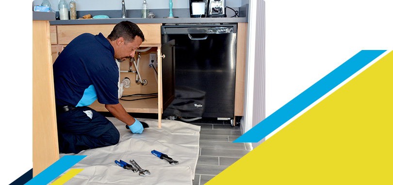 Kneeling Z PLUMBERZ technician inspecting a dishwasher